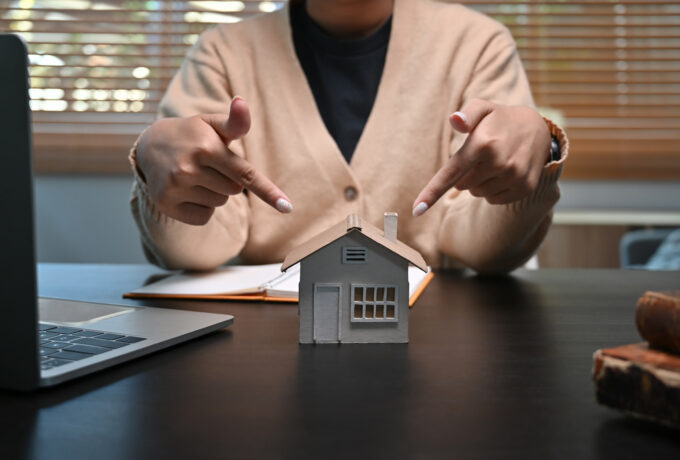 Young woman pointing to house model on table. Mortgage and real estate investment concept.