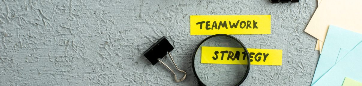 Top view of coloured envelopes and teamwork strategy writings on magnifying glass spiral notebook on gray sand background